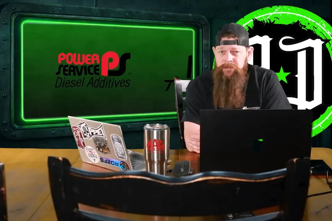 Presenter at a desk with laptop and a green screen displaying the 'Power Service Diesel Additives' logo